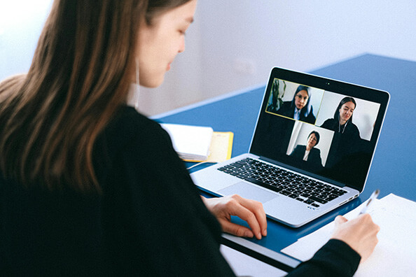 A woman sitting in front of a laptop, engaged in a video conference with three other women displayed on the screen. The women on the screen represent virtual collaboration, showcasing professionals interacting remotely through video conferencing technology